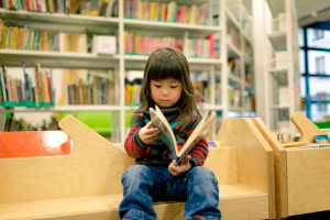 little girl in a library reading a book